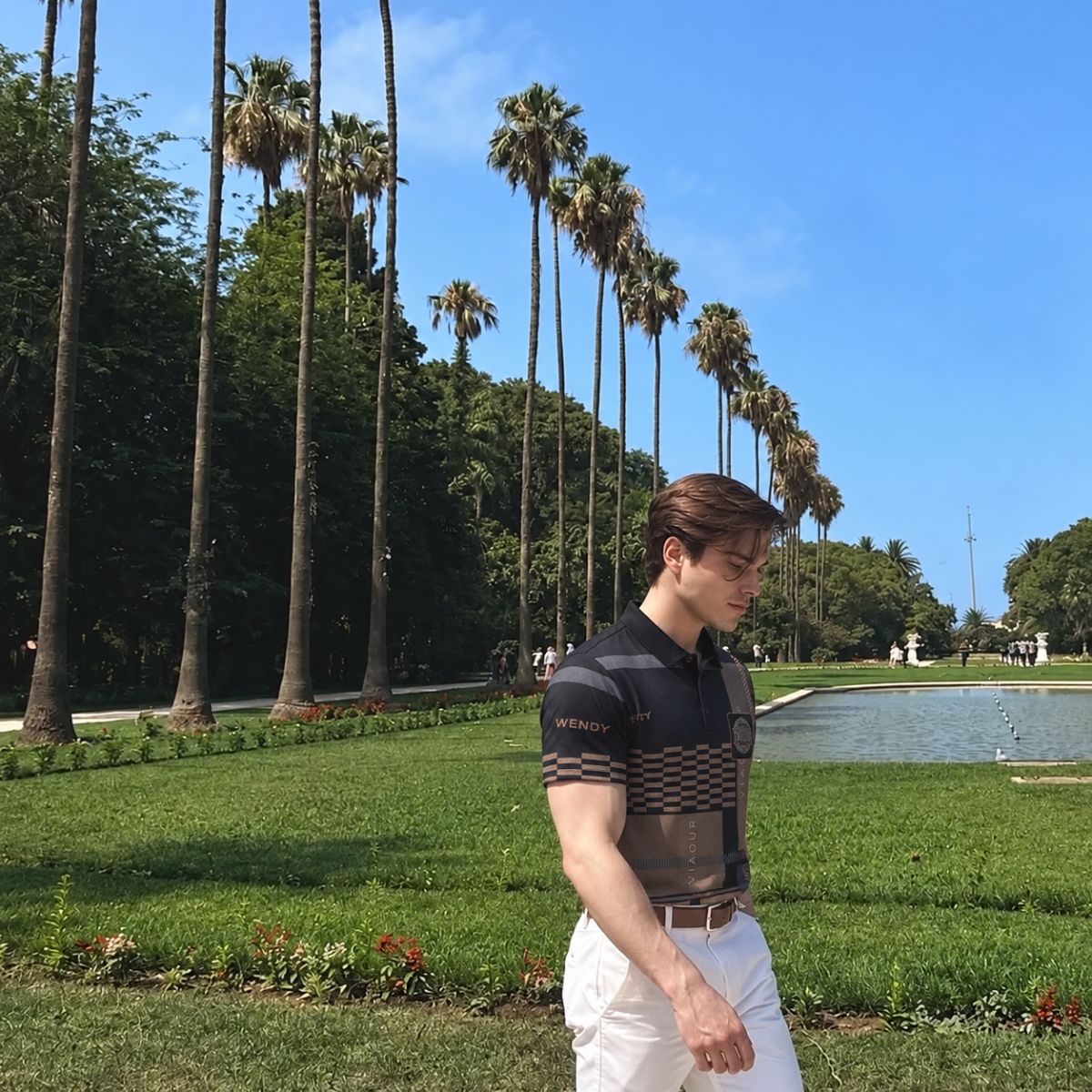 Homem caminhando em parque com camisa polo estampada preta e marrom e calça branca