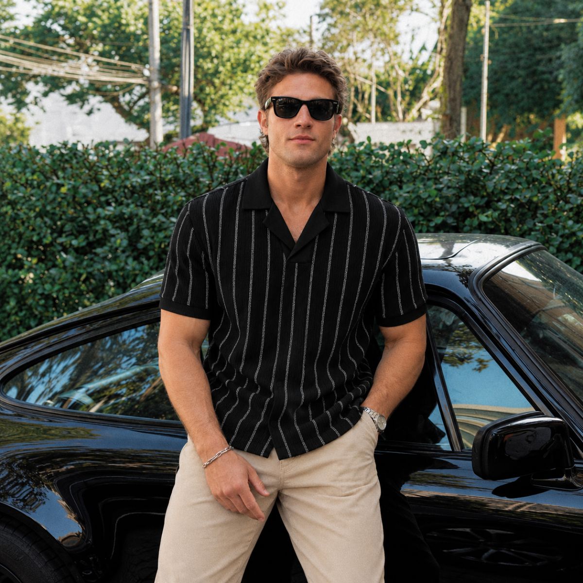 Modelo com Camisa Polo Masculina Listrada Preta Havana e calça bege, encostado em carro