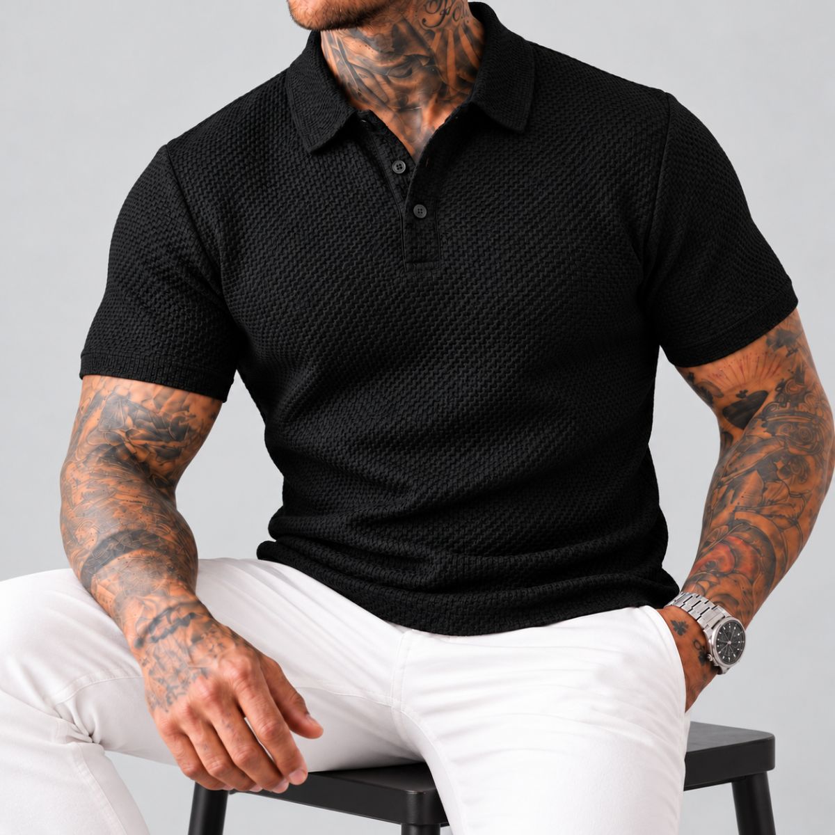 Modelo sentado com camisa polo preta texturizada de seda gelada e calça branca