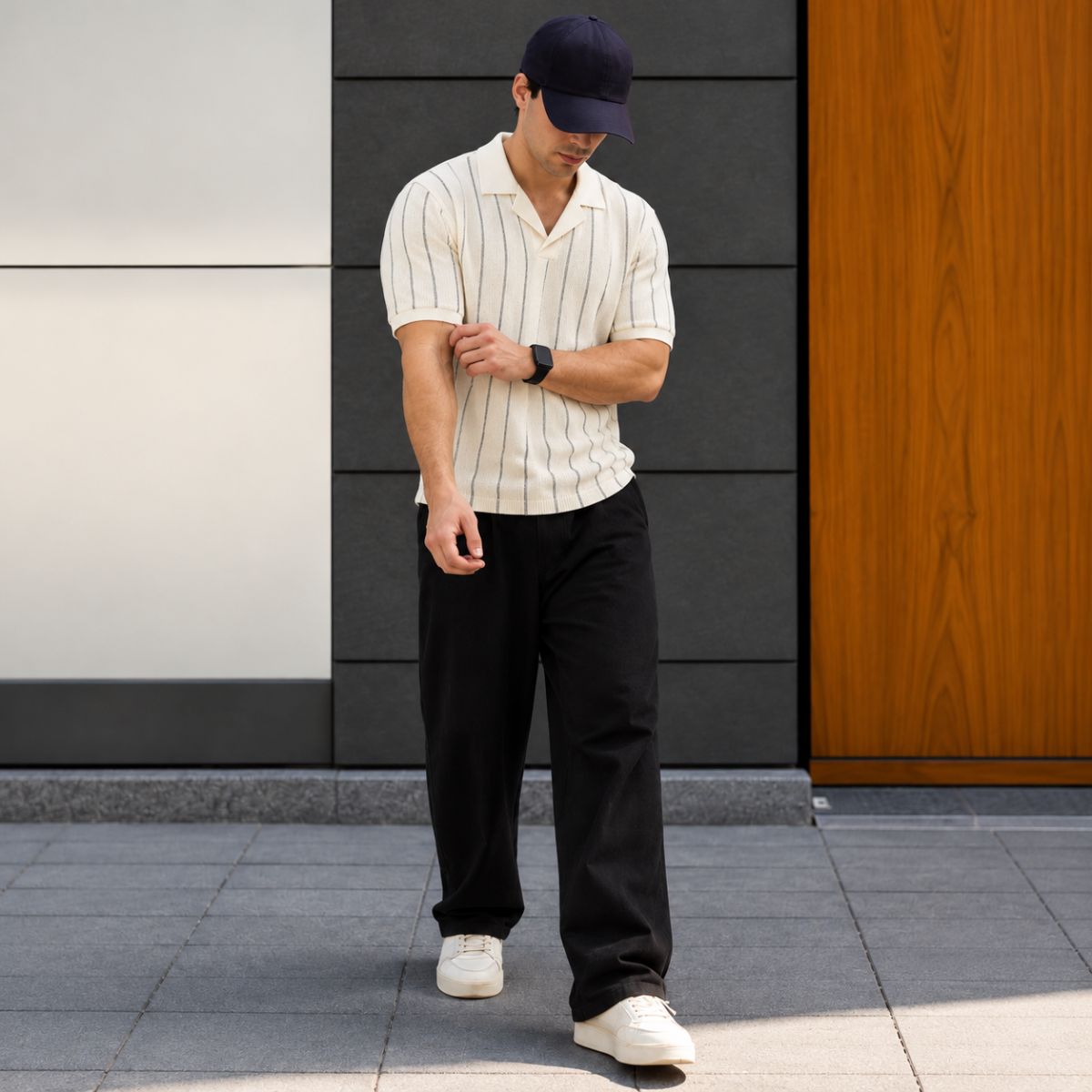 Homem caminhando com camisa polo bege listrada, calça preta e boné, corpo inteiro