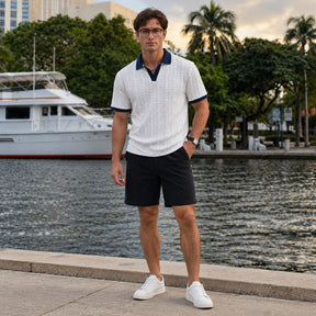 Homem usando camisa polo branca texturizada com bermuda preta e tênis branco, corpo inteiro