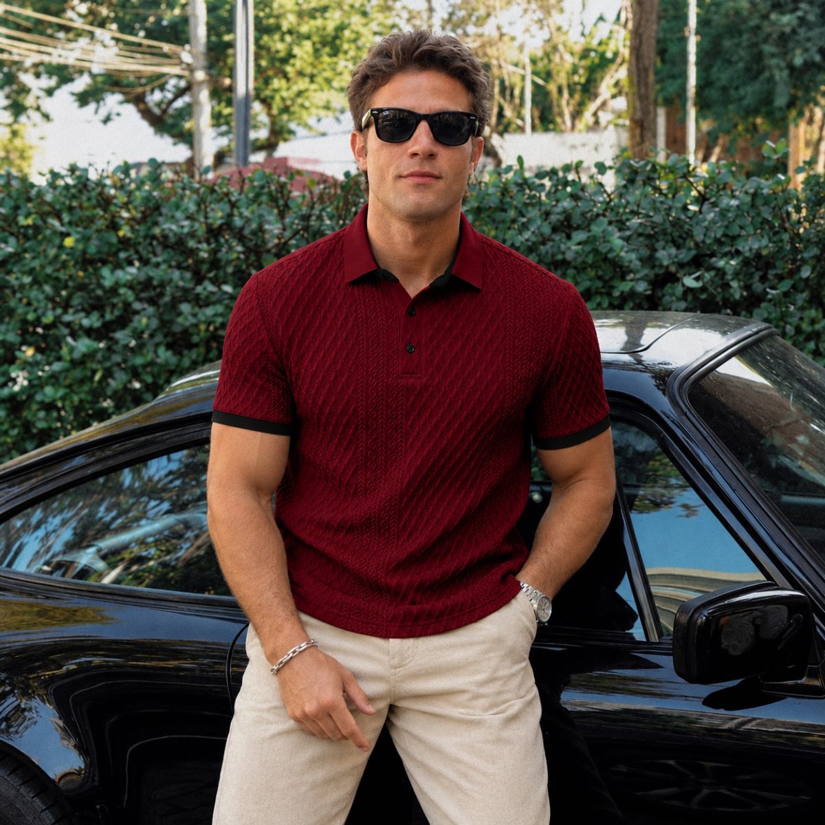 Modelo com camisa polo vinho bordô e calça bege, encostado em carro preto